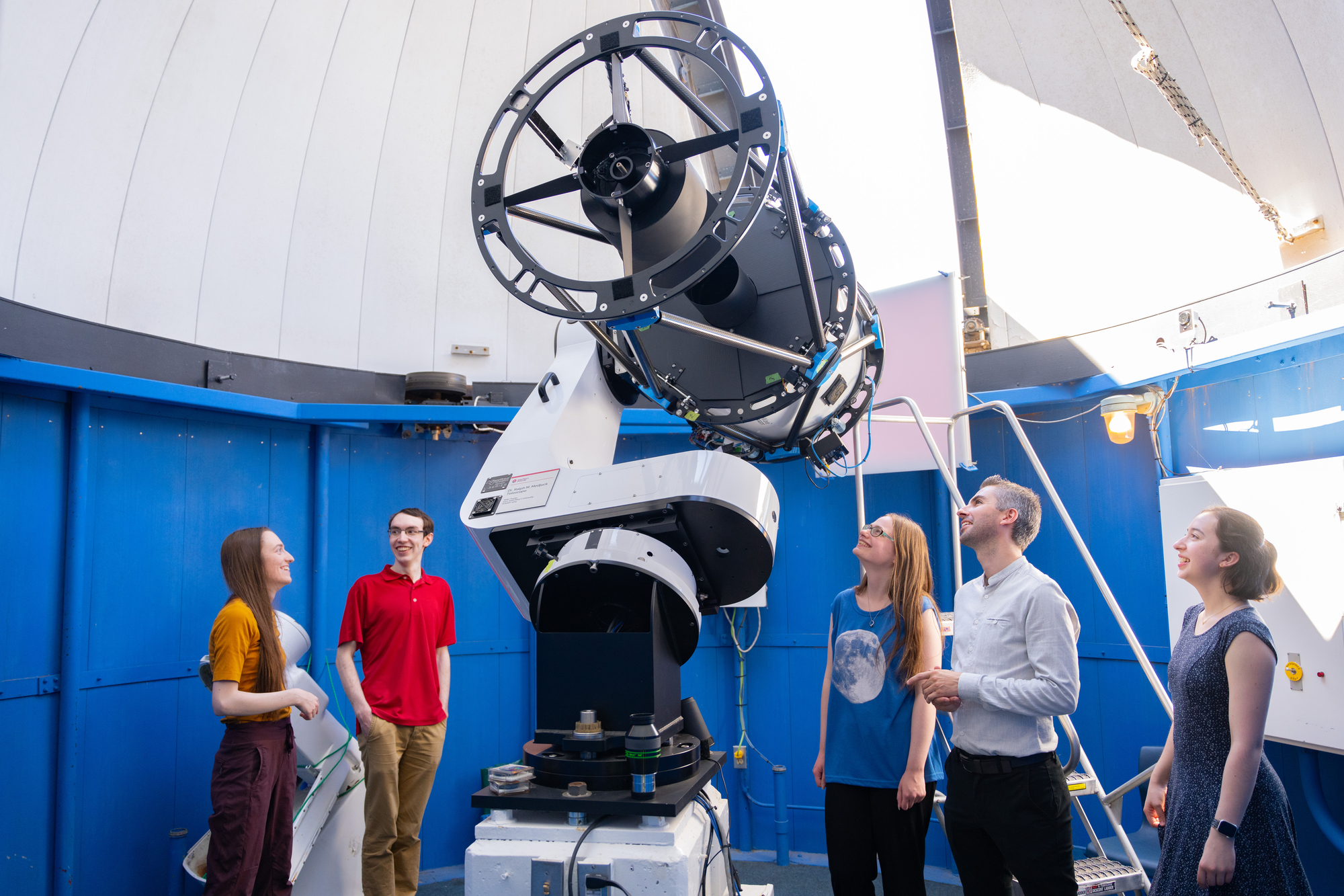Image of a group standing inside the Burke-Gaffney Observatory dome under the telescope in the daytime.
