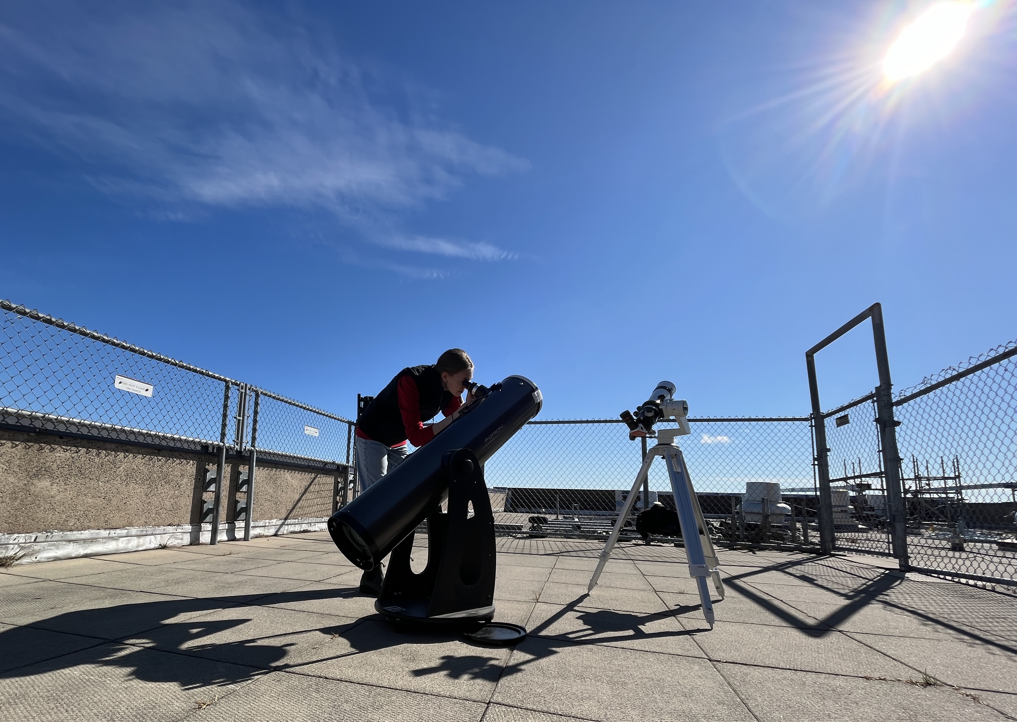 Undergraduate student Katherine Myers using the Burke-Gaffney Observatory rooftop observation to observe the sun safely through a Dobsonian telescope with a solar filter. A dedicated H-alpha solar telescope is also seen on the roof.