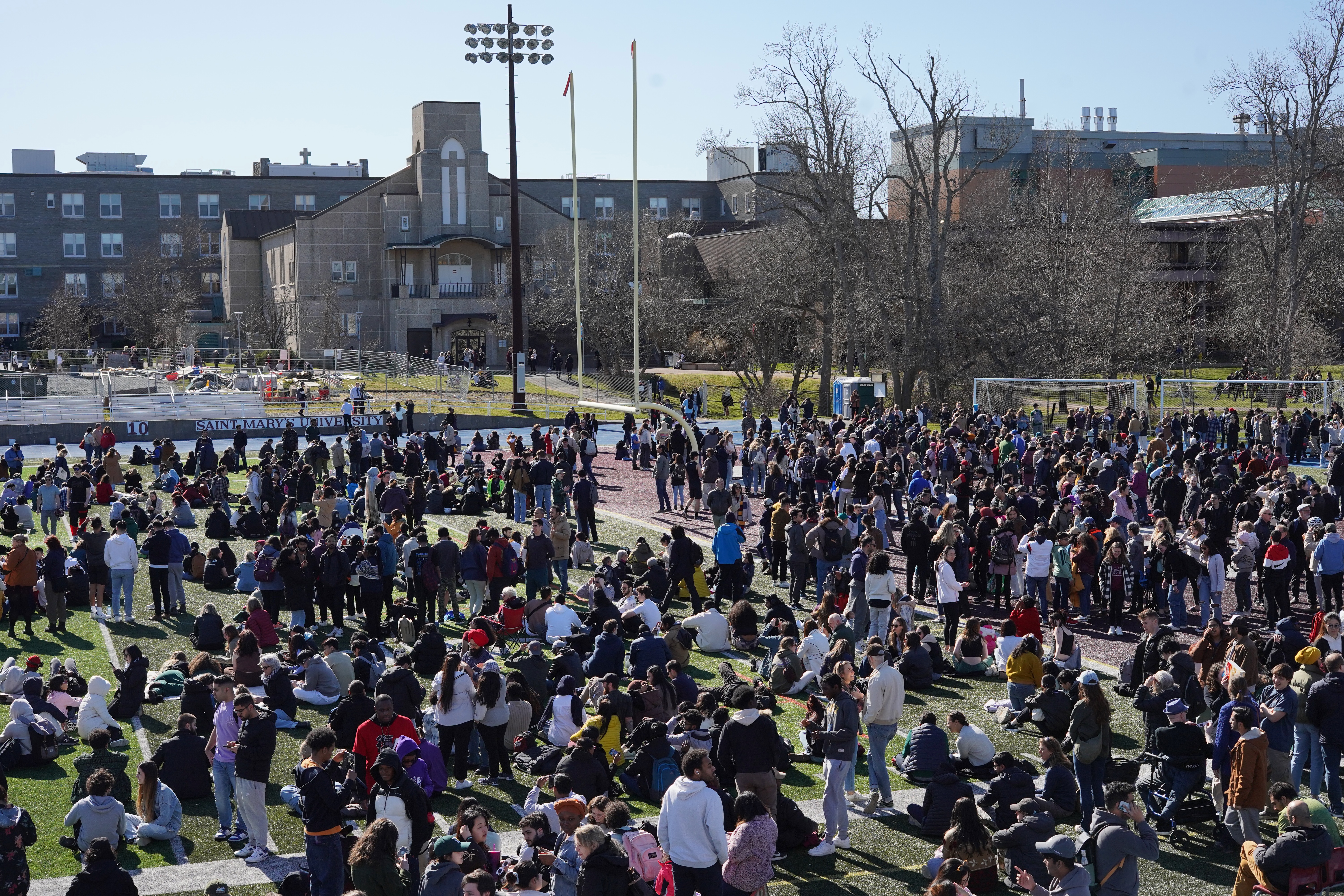 Image of a large crowd gathered on the football field at SMU under clear blue skies.