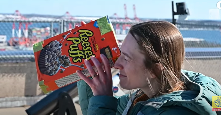 Image of woman outdoors looking down the end of a cereal box with her back towards the sun.